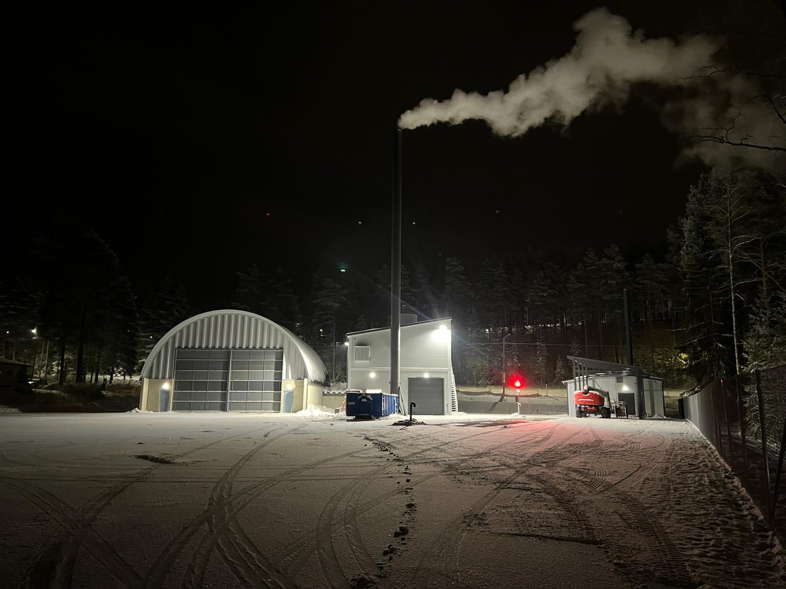 Lämpökeskus talvi-illan pimeässä. Polttoainevarasto vasemmalla.